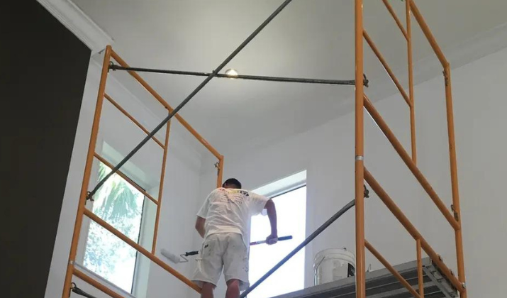 Painter working on an interior ceiling from scaffolding